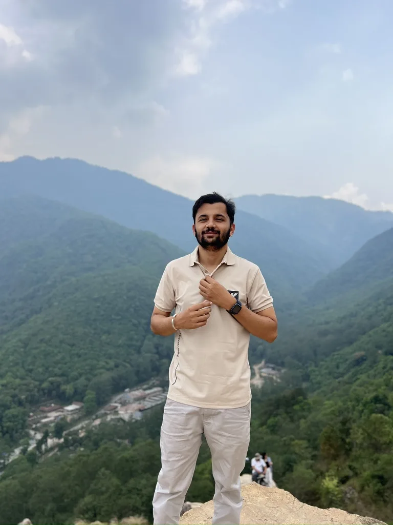 Prajwal Giri standing on a rocky lookout above green hills